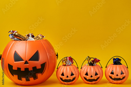 Parents and kids Halloween concept. Big Pumpkin head basket with three small baskets full of candy over yellow background and copyspace photo