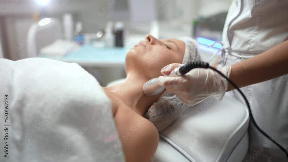 Lovely caucasian female getting RF lifting, skin tightening procedure of neckline area at cosmetology clinic. Non surgery, hardware cosmetology, professional skincare, beauty treatment concept. Lovely caucasian female getting RF lifting, skin tightening procedure of neckline area at cosmetology clinic. Non surgery, hardware cosmetology, professional skincare, beauty treatment concept.