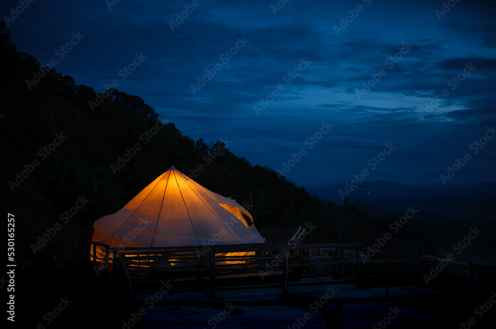 Tent Camping glows on mountain peak at blue twilight evening, travel and nature concept