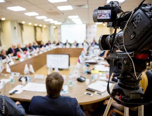 People sitting at a round table in the negotiations in the conference room. In the foreground TV video equipment for shooting