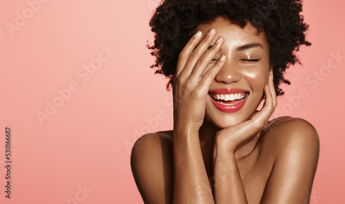 Skin care. Woman with beauty face touching healthy facial skin portrait. Beautiful African girl model with natural makeup touching glowing hydrated skin on pink background closeup