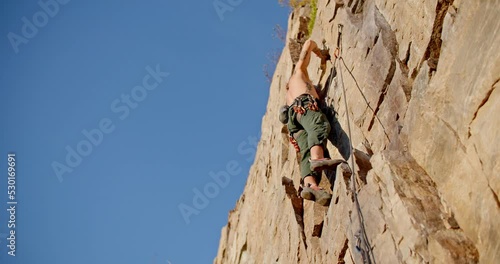 Male rock climber chalks up on wall, takes step