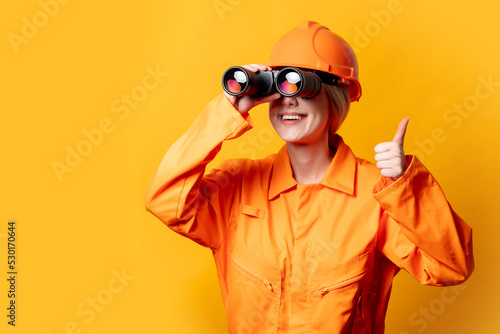 worker in helmet and orange overalls with binocular