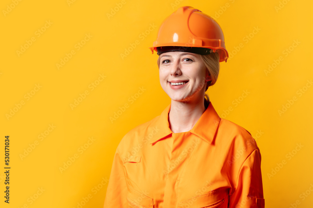 Stylish blond hair worker woman in orange helmet and suit on yellow background