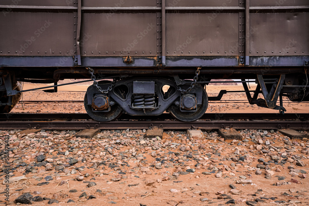 Old cargo train at Wadi Rum desert station, red sand and dust near railroad tracks, closeup detail from side