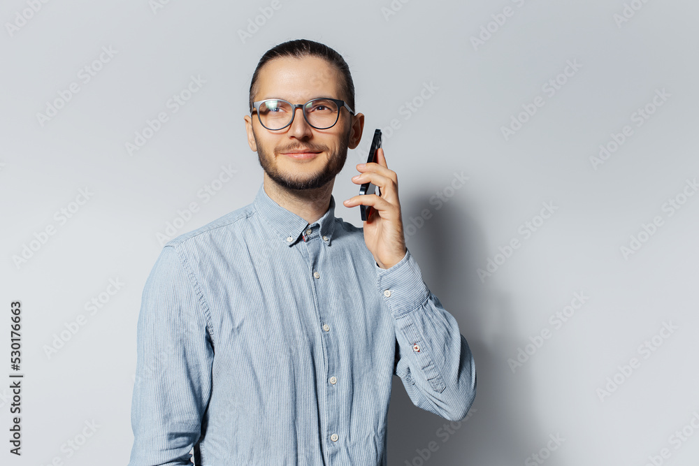 Studio portrait of young smiling man talking on smartphone, wearing eyeglasses and blue shirt on white background. Studio portrait of young smiling man talking on smartphone, wearing eyeglasses and blue shirt on white background.