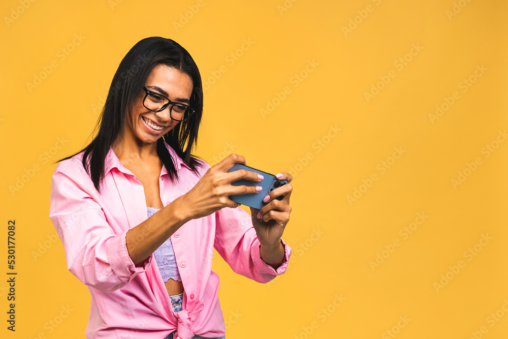 Portrait of her she nice attractive lovely cheerful african american black girl holding in hands mobile phone chatting on web isolated over yellow background. Play phone games, using mobile apps. Portrait of her she nice attractive lovely cheerful african american black girl holding in hands mobile phone chatting on web isolated over yellow background. Play phone games, using mobile apps.