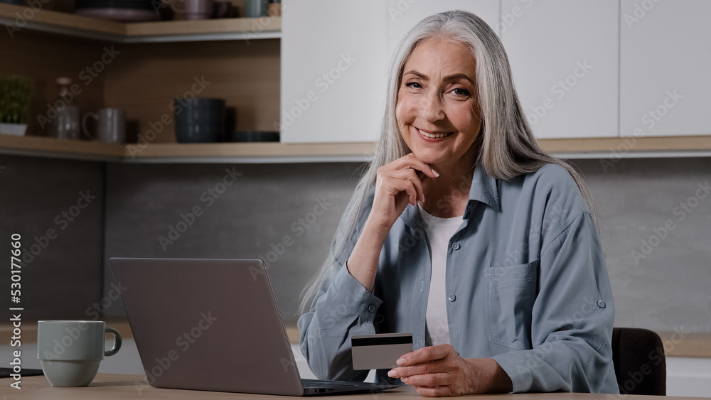 Elderly lady buyer grandmother shopper mature woman sit in kitchen pay utility bills on laptop use banking app for online charity enter security card number at computer internet financial transaction Elderly lady buyer grandmother shopper mature woman sit in kitchen pay utility bills on laptop use banking app for online charity enter security card number at computer internet financial transaction