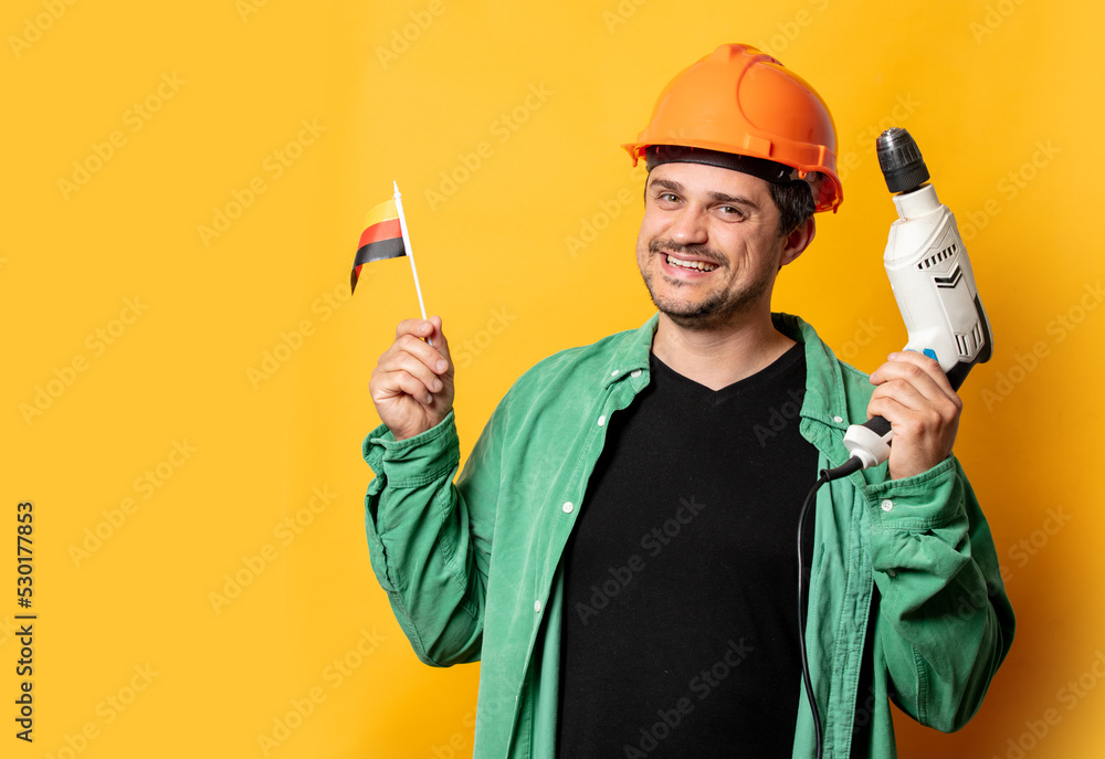 Guy in helmet with drill and German flag on yellow background Guy in helmet with drill and German flag on yellow background