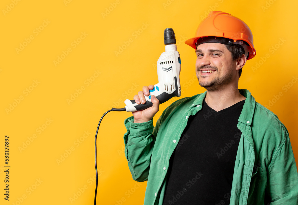 Guy in helmet with drill on yellow background Guy in helmet with drill on yellow background