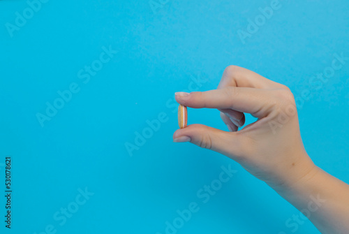 A woman holds a headache pill in her hand on a blue background, vitamins or medicine. Treatment from virus, disease. Health care, medicine.