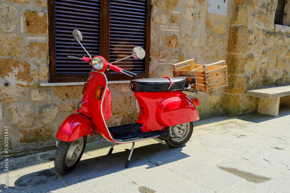 Pitigliano, Italy - July 31  2022: Iconic red Vespa motorbike parked in the street of Pitigliano in Tuscany, Italy