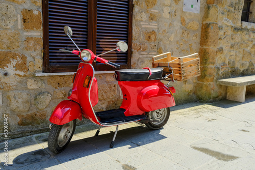 Pitigliano, Italy - July 31  2022: Iconic red scooter motorbike parked in the street of Pitigliano in Tuscany, Italy