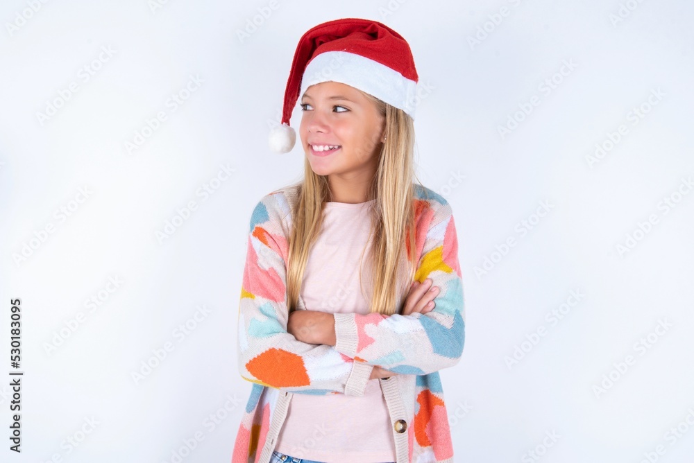 Dreamy rest relaxed little kid girl with Christmas hat wearing yarn jacket over white background crossing arms, looks good copyspace Dreamy rest relaxed little kid girl with Christmas hat wearing yarn jacket over white background crossing arms, looks good copyspace