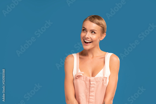 Photo of cheerful woman with short blonde hairstyle, smiling, posing on blue studio background. Copy space.