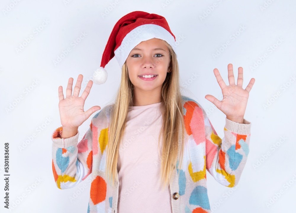 little kid girl with Christmas hat wearing yarn jacket over white background showing and pointing up with fingers number ten while smiling confident and happy. little kid girl with Christmas hat wearing yarn jacket over white background showing and pointing up with fingers number ten while smiling confident and happy.