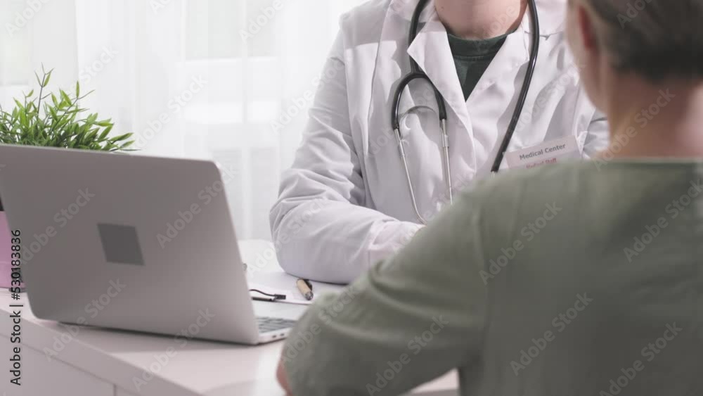 female doctor talking to woman patient during appointment in clinic office. medicine worker in lab coat sitting at white table explaining patient. physician takes patient's hand telling bad news female doctor talking to woman patient during appointment in clinic office. medicine worker in lab coat sitting at white table explaining patient. physician takes patient's hand telling bad news