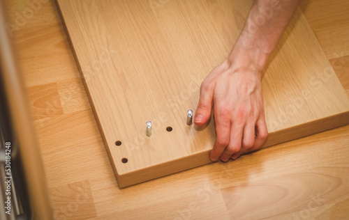 The hand of a caucasian young man takes the wooden part of the bed from the floor