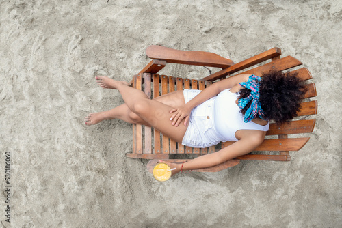 Young woman sitting on deck chair at beach during summer vacation © Andrés Rivas