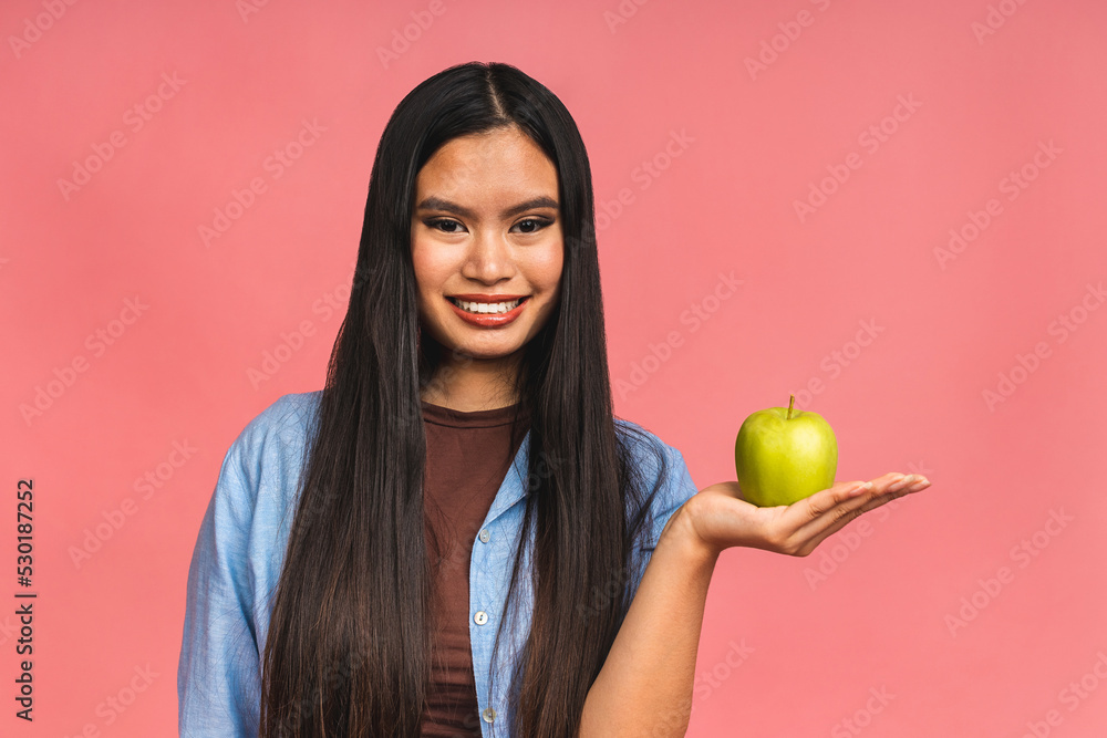 Portrait of a happy young asian chinese korean japanese woman holding or eating green apple isolated over pink background. Portrait of a happy young asian chinese korean japanese woman holding or eating green apple isolated over pink background.