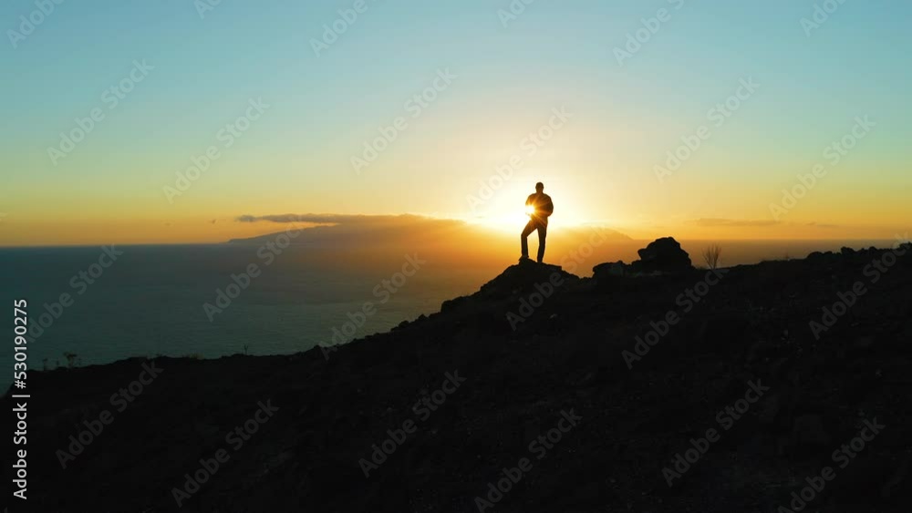 Silhouette of man on mountain top at sunset. Aerial. Sun sets on La Gomera. Atlantic ocean. Striking precipice. Tenerife, Canary Island, Spain. Travel destination. Go everywhere. Silhouette of man on mountain top at sunset. Aerial. Sun sets on La Gomera. Atlantic ocean. Striking precipice. Tenerife, Canary Island, Spain. Travel destination. Go everywhere.