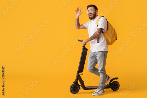 Handsome tattooed student with kick scooter on yellow background photo