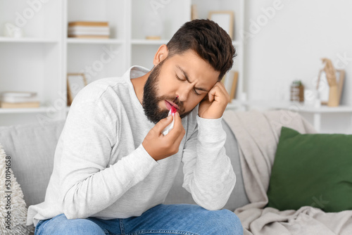 Young bearded man with nosebleed and tissue at home