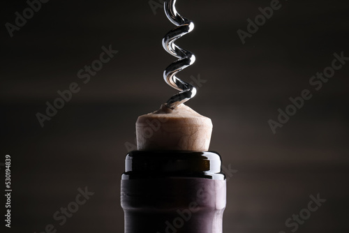 Opening wine bottle with corkscrew on dark background, closeup photo
