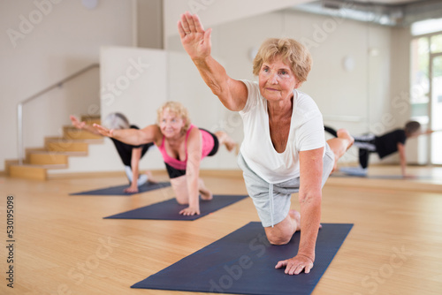 Positive senior woman practicing Balancing Table pose (Dandayamna Bharmanasana) to improve balance, coordination and core strength during group yoga training