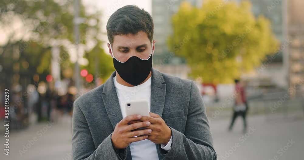 Young Businessman Using Cloth Face Mask Thinking And Texting Using a Smartphone. He is Checking The News or Chatting with Friends. Slow Motion Shot, City Background
Young Businessman Using Cloth Face Mask Thinking And Texting Using a Smartphone. He is Checking The News or Chatting with Friends. Slow Motion Shot, City Background