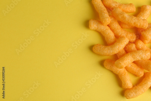 Tasty cheesy corn puffs on yellow background, flat lay. Space for text