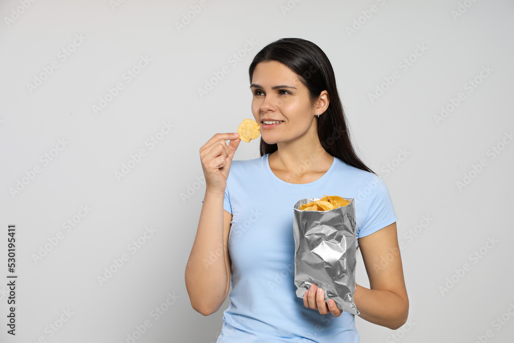 Beautiful woman eating potato chips on grey background. Space for text Beautiful woman eating potato chips on grey background. Space for text