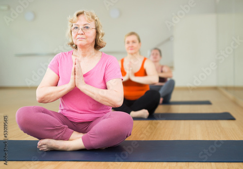 Mature woman maintaining mental and physical health attending group yoga class at studio, practicing breathing exercises and meditation