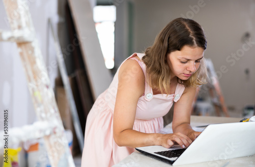 Young woman construction manager using laptop while working in apartment. Home improvement.