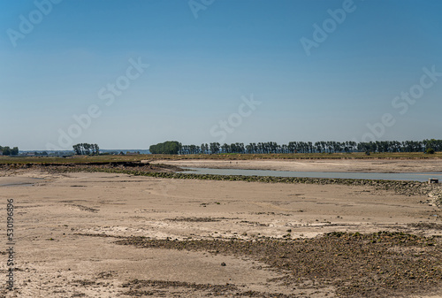 Mont St. Michel, Normandy, France - July 8, 2022: Landscape with flat low tide beach and green marsh under blue sky with green tree line on horizon.