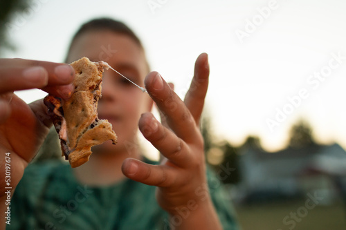 boy eating smore with marshmallow sticking to his fingers at a summer campfire