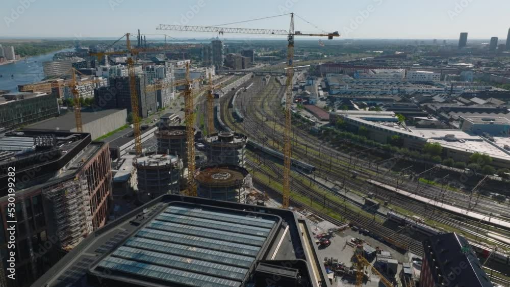 Forwards fly around group of tall tower cranes on high rise building construction site. Train driving on railway tracks in city. Copenhagen, Denmark Forwards fly around group of tall tower cranes on high rise building construction site. Train driving on railway tracks in city. Copenhagen, Denmark
