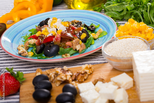 Fresh ingredients for preparation of vitamin salad from arugula and vegetables on striped textile background..