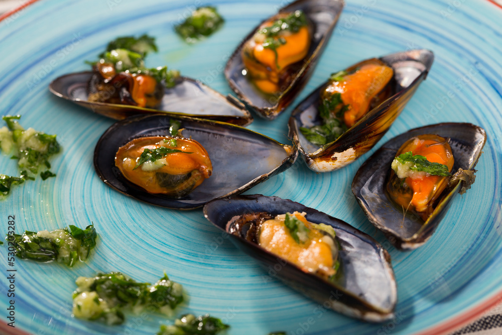 Gourmet steamed mussels served with sauce of oil, garlic and parsley on blue plate..