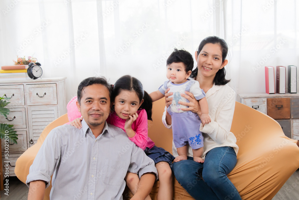 Selective focus Asian happy family sitting on cozy sofa cuddling with two little children take a photo in living room. Sibling with mom and dad spend time together in holiday, family enjoy free time. Selective focus Asian happy family sitting on cozy sofa cuddling with two little children take a photo in living room. Sibling with mom and dad spend time together in holiday, family enjoy free time.