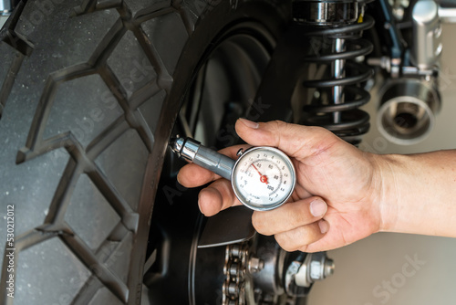 Foto Man holding pressure gauge for checking  motocycle tyre pressure ,maintenance,repair motorcycle concept in garage