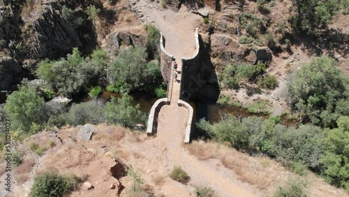 Birds eye top view as people crossing an old brick foot bridge over a stream. Aerial still shot. photo