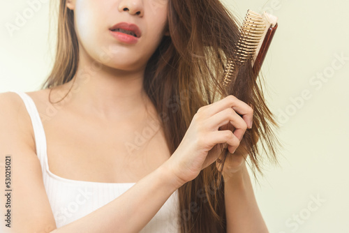 Damaged Hair, frustrated asian young woman, girl hand in holding brush splitting ends messy while combing hair, unbrushed dry long hair. Health care beauty, portrait isolated on white background.