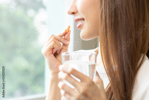Schilderij op canvas Dietary supplement, asian young woman, girl hand holding orange medical pill, take or eat vitamin C, D for treatment for skin, hair and nail strengthen with glass of pure water at home, healthcare