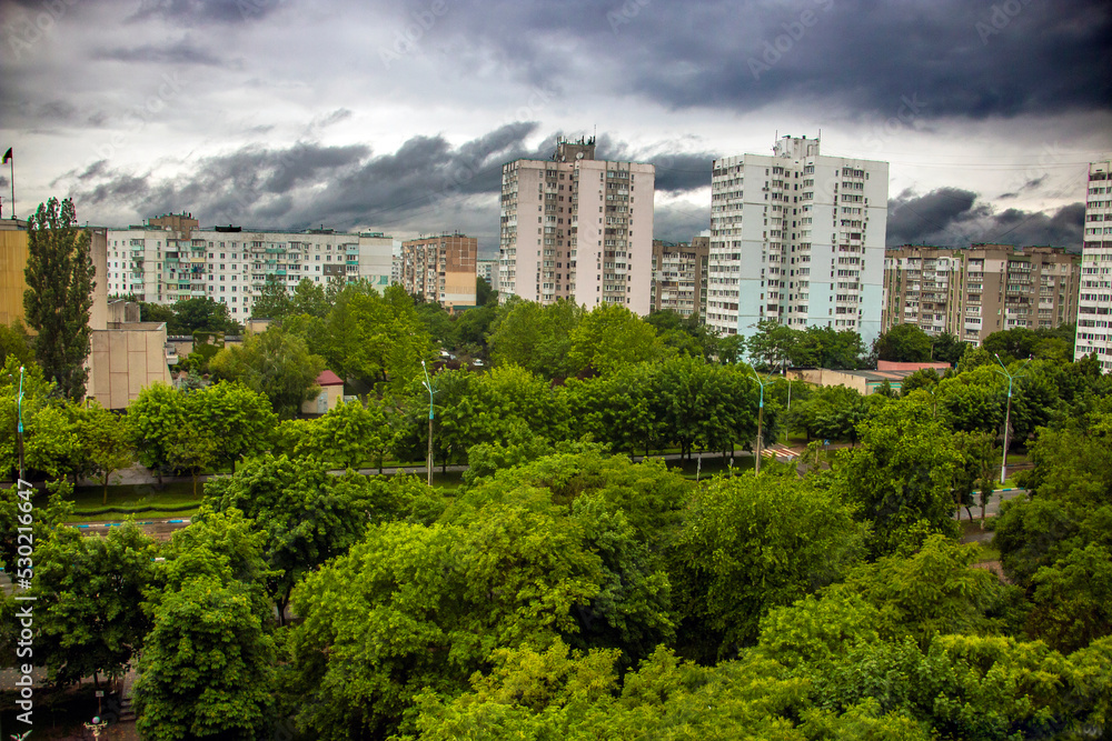 Nine-story and sixteen-story houses among green plants in the city from a height under a blue sky with white clouds