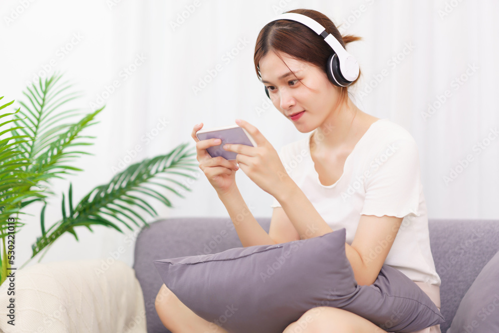 Lifestyle in living room concept, Young Asian woman in headphone to playing games on smartphone Lifestyle in living room concept, Young Asian woman in headphone to playing games on smartphone