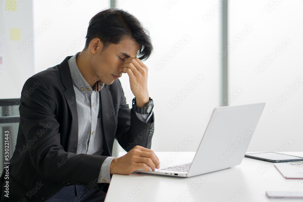 Young asian businessman in black suit massages between eyes with fingers. The concept of unemployed, sadness, depressed and human problems. Young asian businessman in black suit massages between eyes with fingers. The concept of unemployed, sadness, depressed and human problems.