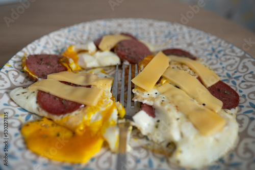 A plate of scrambled eggs with sausage and cheese, with a fork.