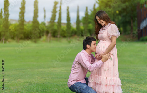 married couple is expecting a baby. man kissing belly of his pregnant wife in park