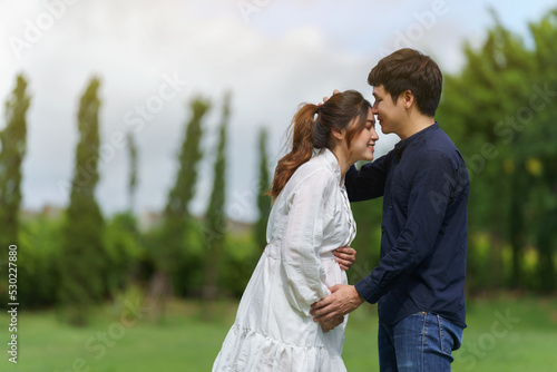 married couple is expecting a baby. man kissing his pregnant wife in park